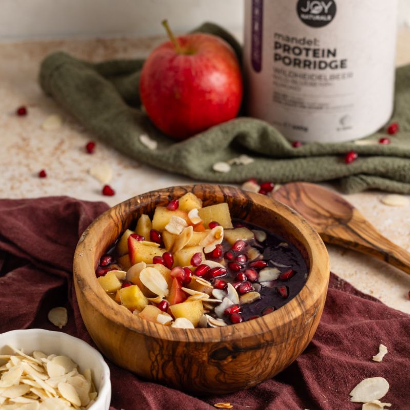 JOY NATURALS Mandel Protein Porridge Wildheidelbeer mit einem Topping aus Apfelstückchen und Granatapfelkernen.