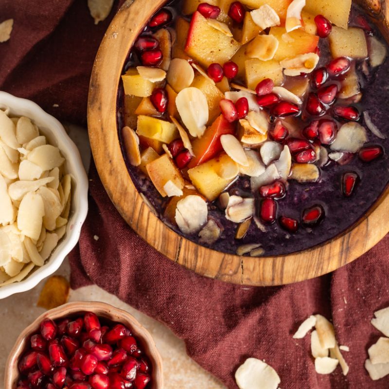 Mandel Protein Porridge Wildheidelbeer von JOY NATURALS, angerichtet mit Apfelstückchen und Granatapfelkernen.